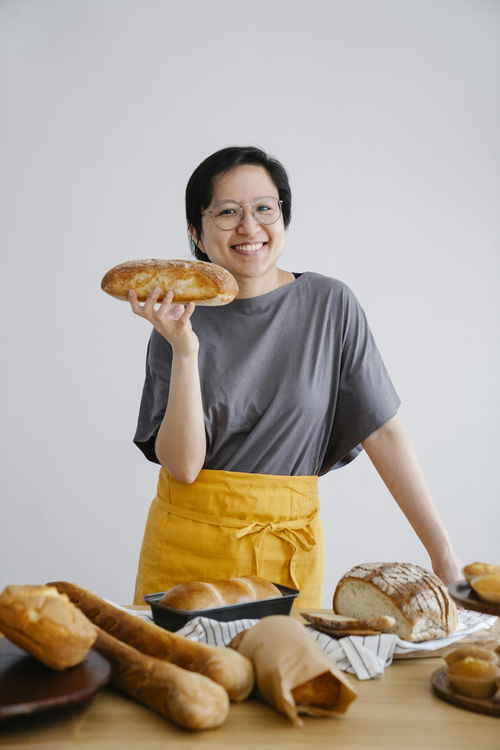 Happy baker holding fresh artisan bread in a sunny kitchen filled with delicious pastries.